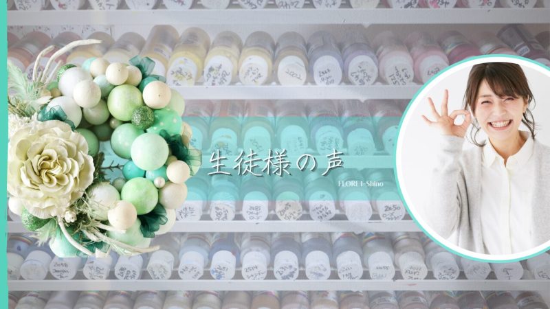 １００種類の絵の具を背景にグリー系のクレイクラフトリースと大輪のバラ１輪、オリジナルタッセルを添えて。笑顔の女性